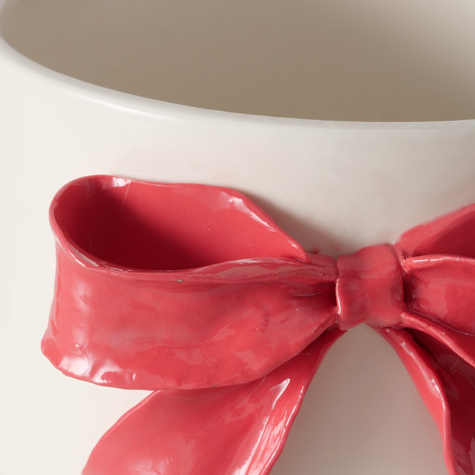 Nahaufnahme eines weißen Übertopfs aus Porzellan mit einer dekorativen roten Schleife auf der Vorderseite.