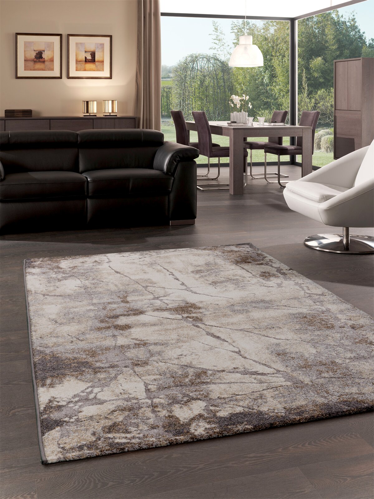 Merinos Kurzflorteppich IBIZA Moderner Wohnzimmerteppich in Beige-, Grau- und Brauntönen mit abstraktem Stein-/Marmor-Muster, in schräger Perspektive von vorne auf dunklem Holzboden vor schwarzem Ledersofa und Essbereich.