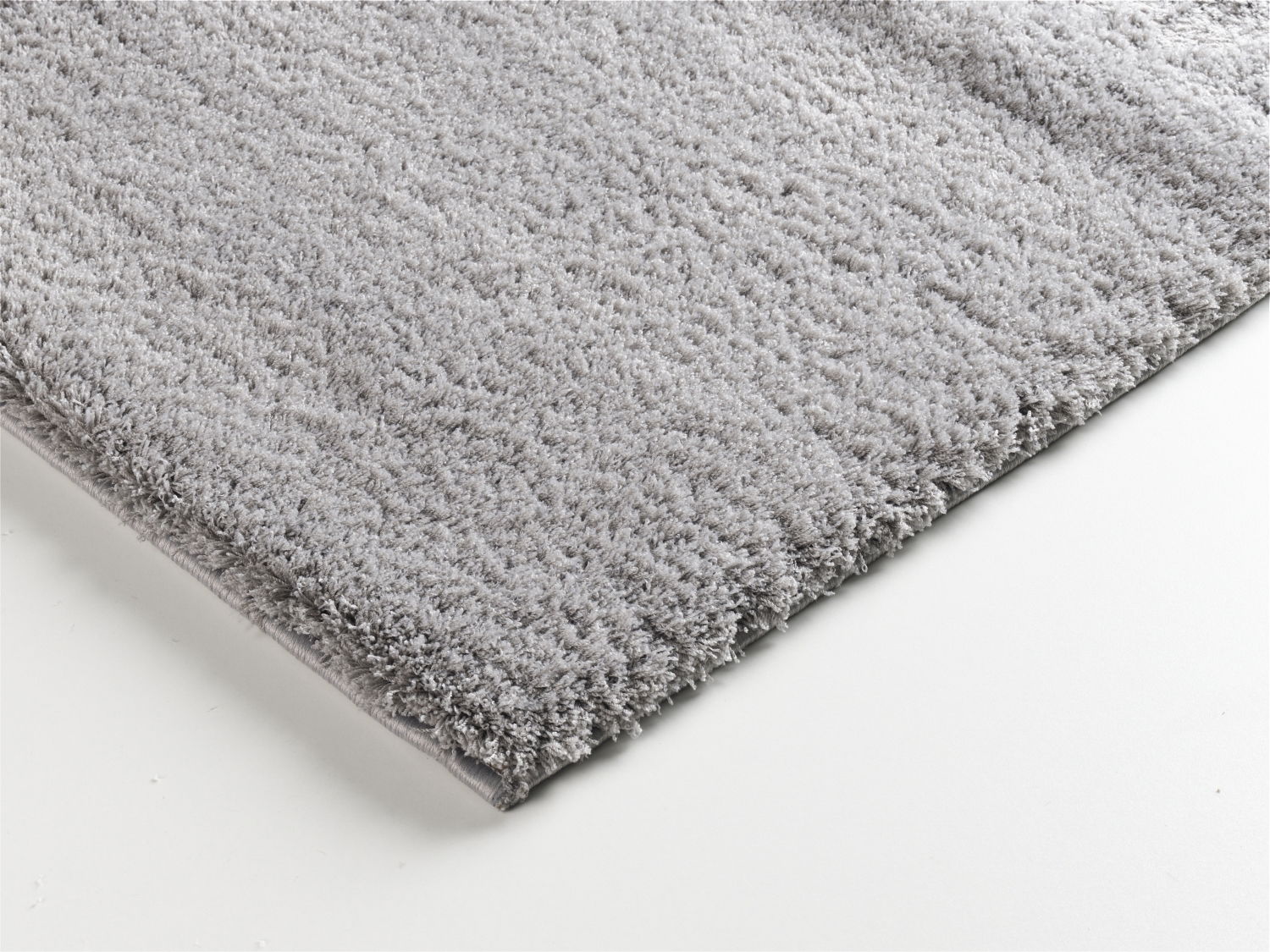 Nahaufnahme eines weichen, grauen Teppichs mit flauschiger Textur, perspektivisch von der Seite aufgenommen.