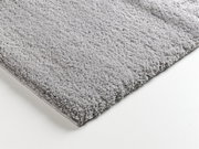 Nahaufnahme eines weichen, grauen Teppichs mit flauschiger Textur, perspektivisch von der Seite aufgenommen.