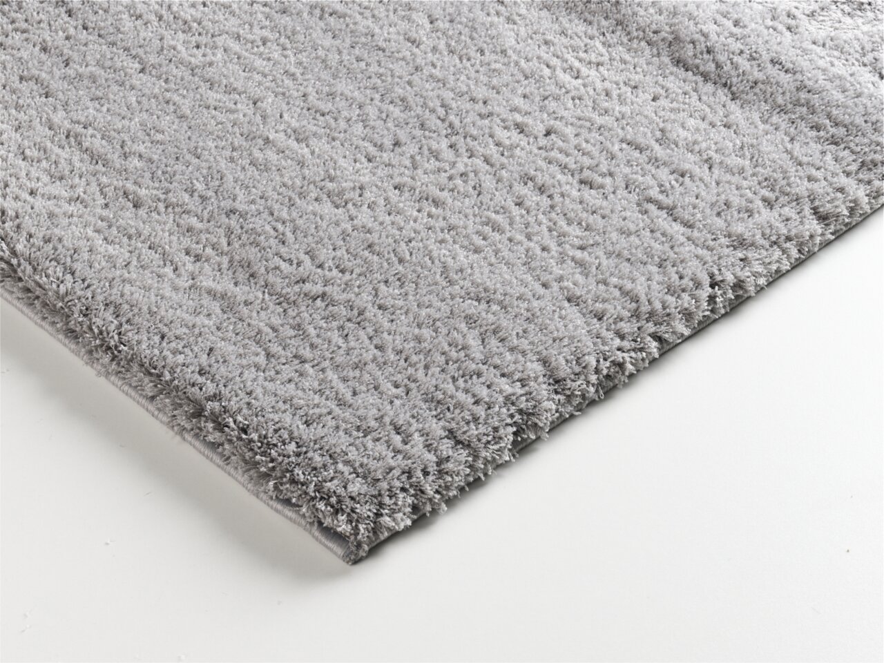 Nahaufnahme eines weichen, grauen Teppichs mit flauschiger Textur, perspektivisch von der Seite aufgenommen.
