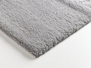 Nahaufnahme eines weichen, grauen Teppichs mit flauschiger Textur, perspektivisch von der Seite aufgenommen.