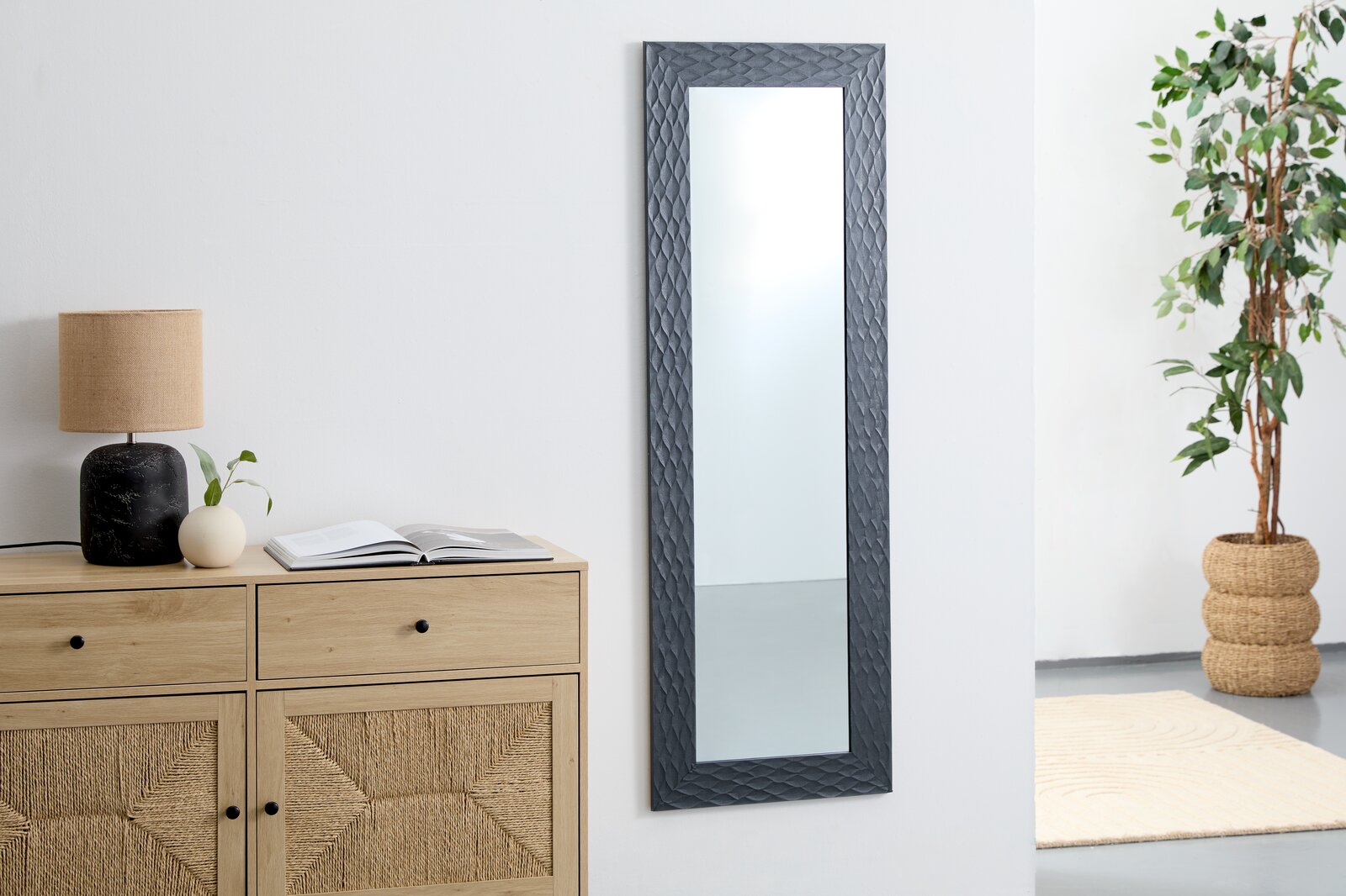 Carryhome Spiegel LUCA Rechteckiger Wandspiegel mit dunklem, strukturiertem Rahmen, aufgehängt in einem modernen Raum mit Kommode, Lampe und Pflanze, seitliche Perspektive.