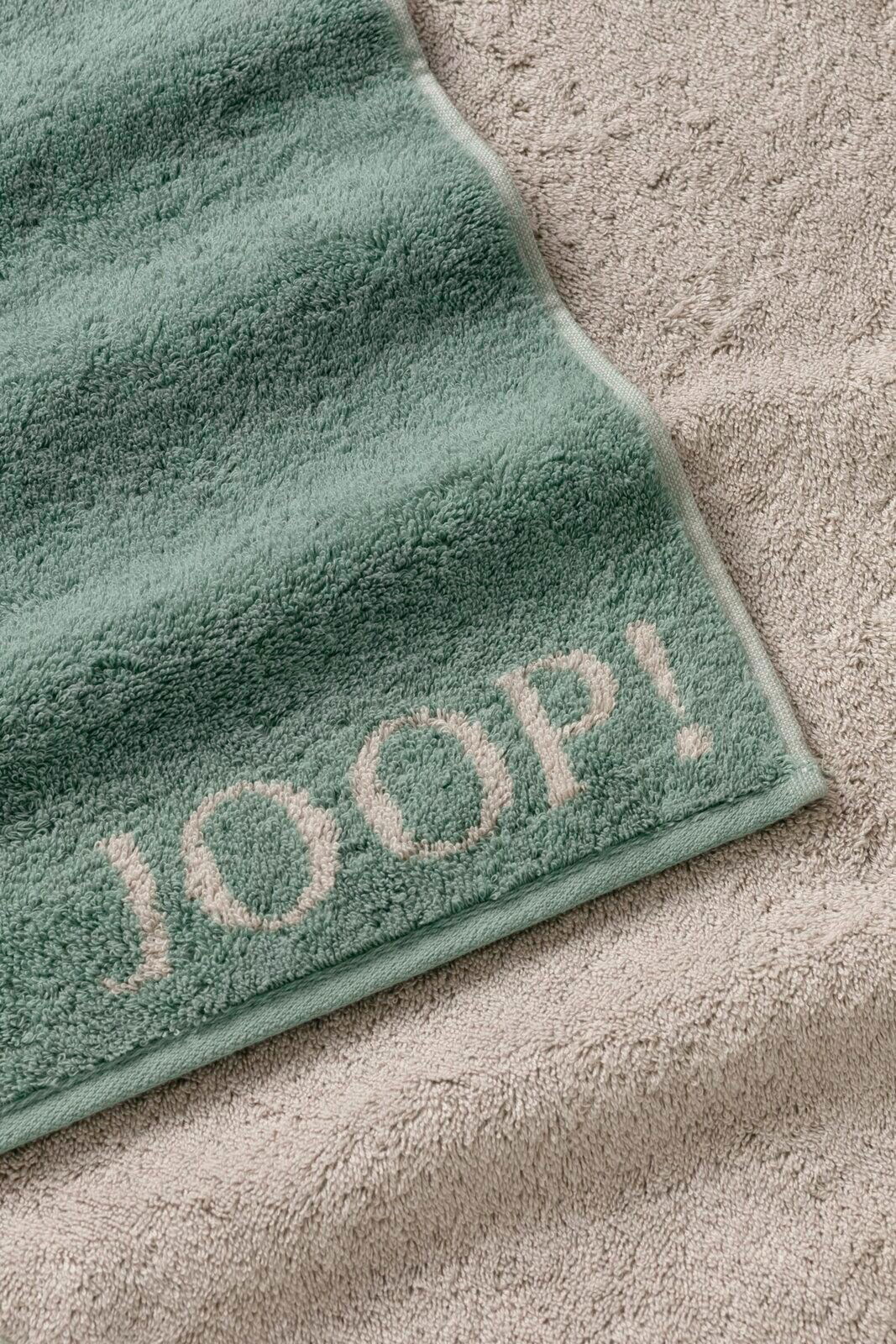 Grünes Handtuch mit dem Schriftzug 'JOOP!' in Nahaufnahme, auf einem beigen Handtuch liegend.