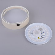 Weiße, runde LED-Deckenleuchte in Einzelteilen (Abdeckring und LED-Platine) auf grauem Hintergrund, schräg von oben fotografiert.
