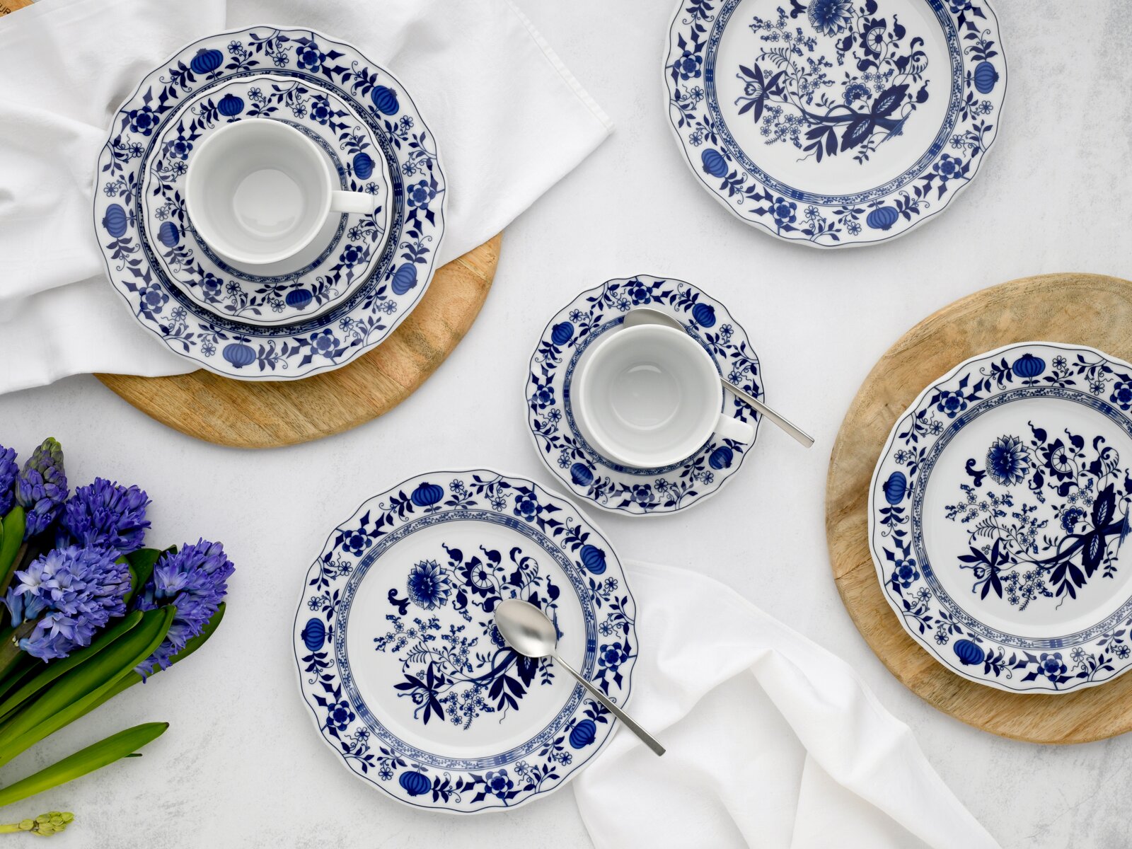 Blau-weißes Porzellan-Geschirrset mit floralen Ornamenten (Tassen mit Untertassen und Teller) auf hellem Tisch mit Holzuntersetzern und weißer Serviette, Draufsicht von oben