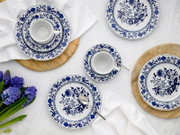 Blau-weißes Porzellan-Geschirrset mit floralen Ornamenten (Tassen mit Untertassen und Teller) auf hellem Tisch mit Holzuntersetzern und weißer Serviette, Draufsicht von oben