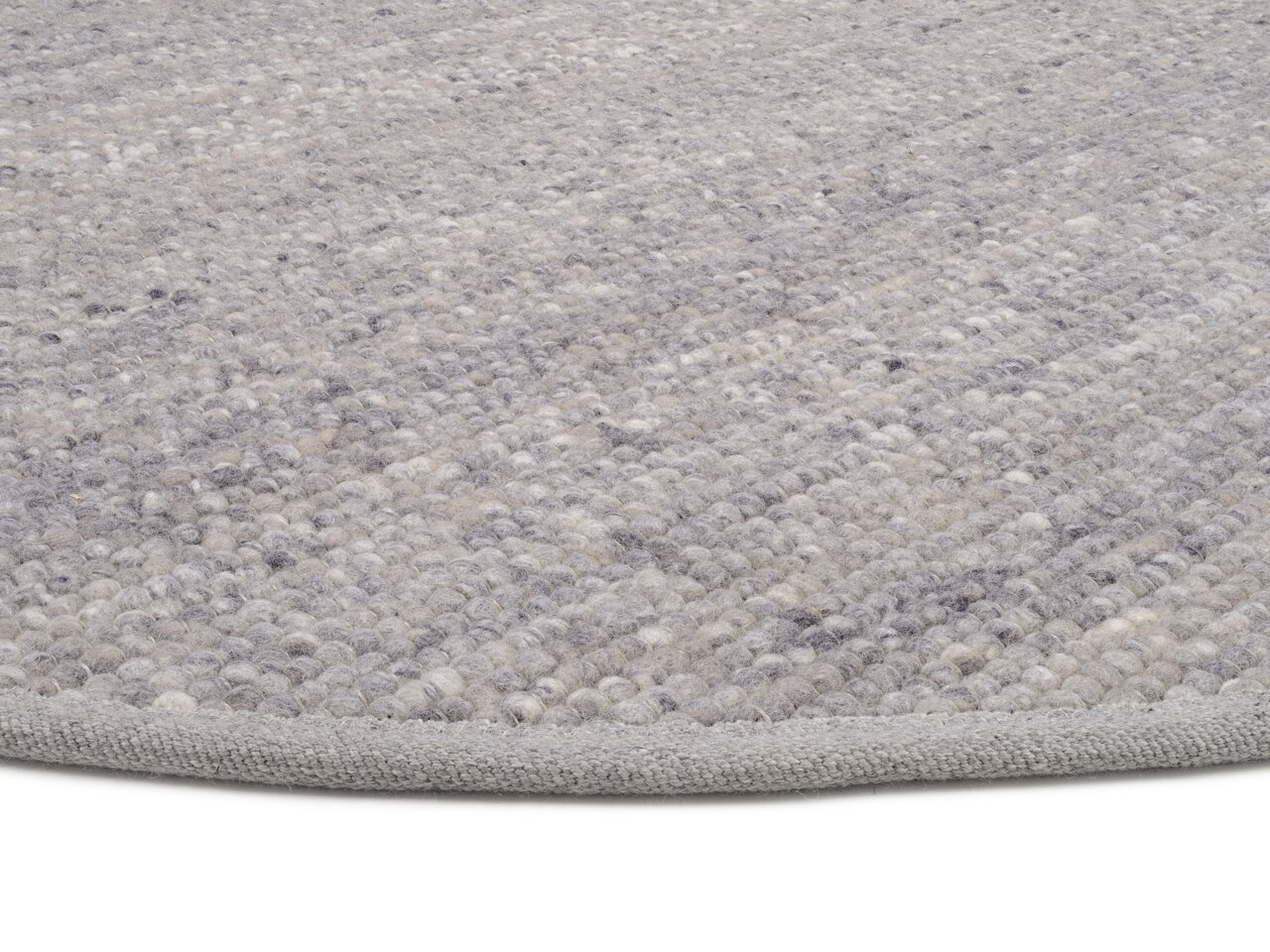 Nahaufnahme eines handgewebten Teppichs in Grautönen, der von der Seite fotografiert wurde.