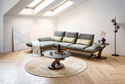Modernes Wohnzimmer mit grauem Ecksofa und gelben Kissen, rundem Couchtisch und Beistelltisch auf hellem Teppich, aufgenommen in schräger Frontansicht aus leicht erhöhter Perspektive.