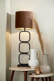 Moderne tafellamp met bruine kap en geometrische metalen voet, gezien vanaf de zijkant, op een tafel met twee decoratieve vazen en een theelichthouder.