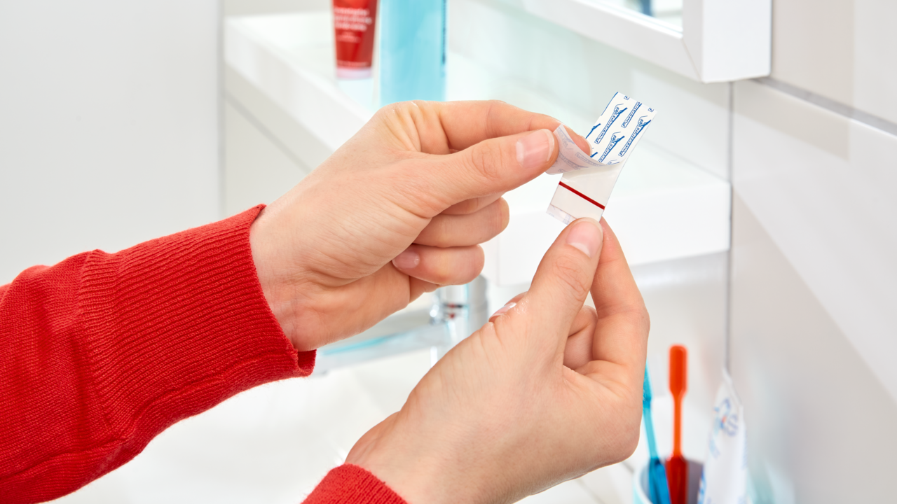 Nahaufnahme von Händen, die einen tesa Powerstrip in einem Badezimmer anbringen.