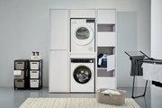 Frontale Ansicht eines modernen Hochschranksystems mit integriertem Waschmaschinen- und Trocknerschrank, umgeben von Wäschekörben und einem Wäscheständer.