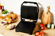 Kontaktgrill Classic GC271D in geöffneter Position auf einer Küchenarbeitsplatte, umgeben von Zutaten wie Brötchen, Salat und Tomaten, aus einer leicht seitlichen Perspektive.