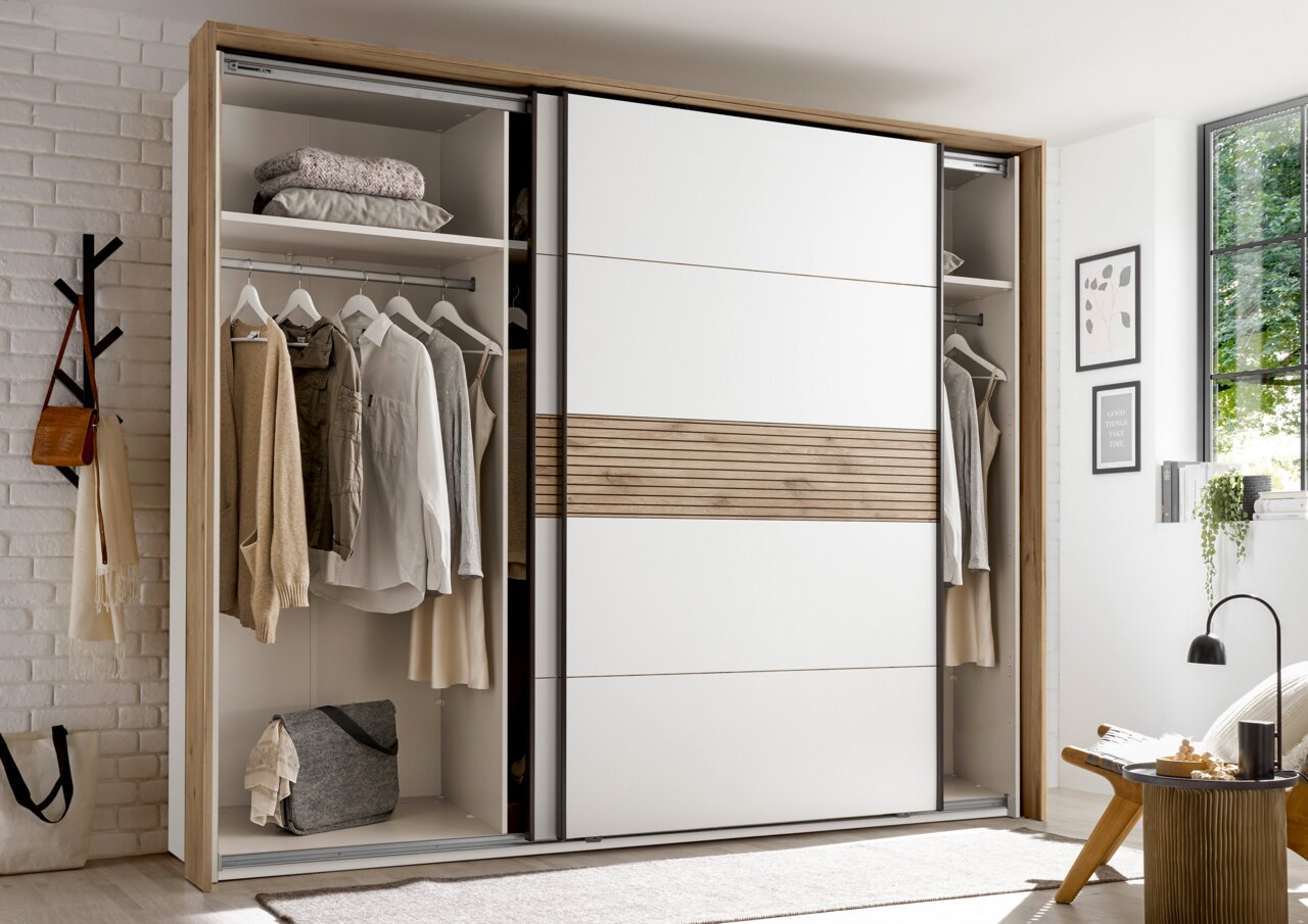 Moderne hangdeurkast met een wit en houtkleurig ontwerp, gedeeltelijk geopend, met daarin kleding en accessoires. Perspectief: vooraanzicht.