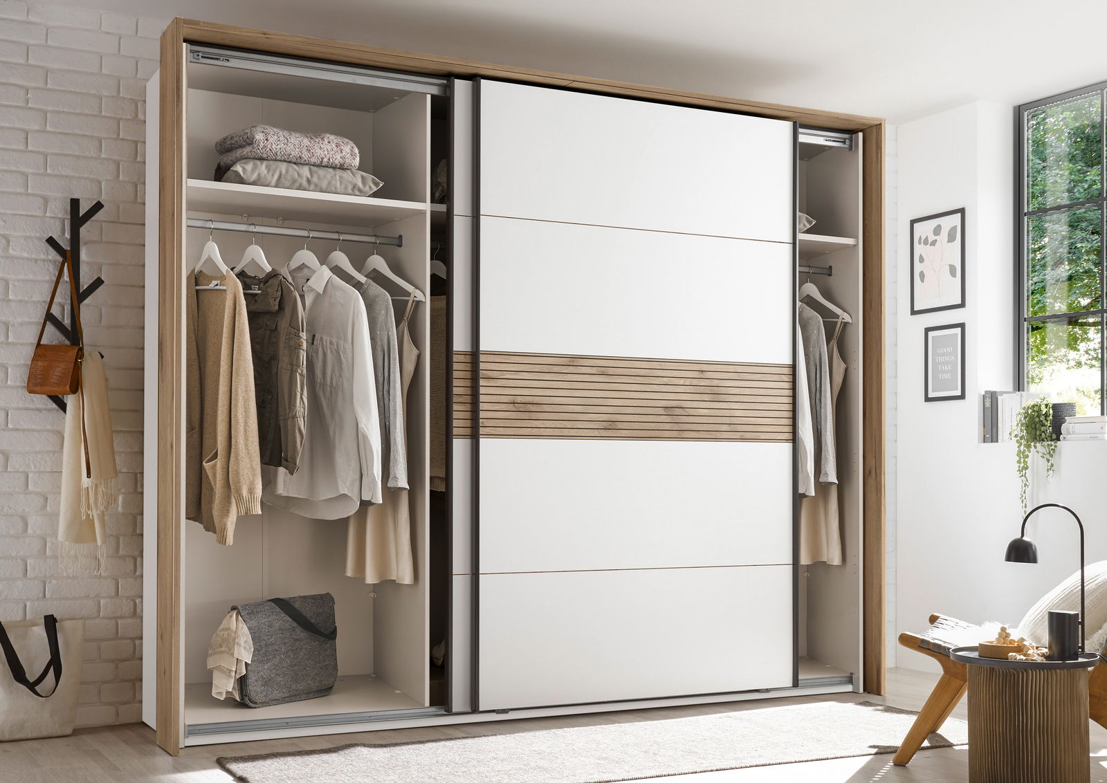 Moderner Schwebetürenschrank mit weißem und holzfarbenem Design, teilweise geöffnet, zeigt Kleidung und Accessoires im Inneren. Perspektive: Frontalansicht.