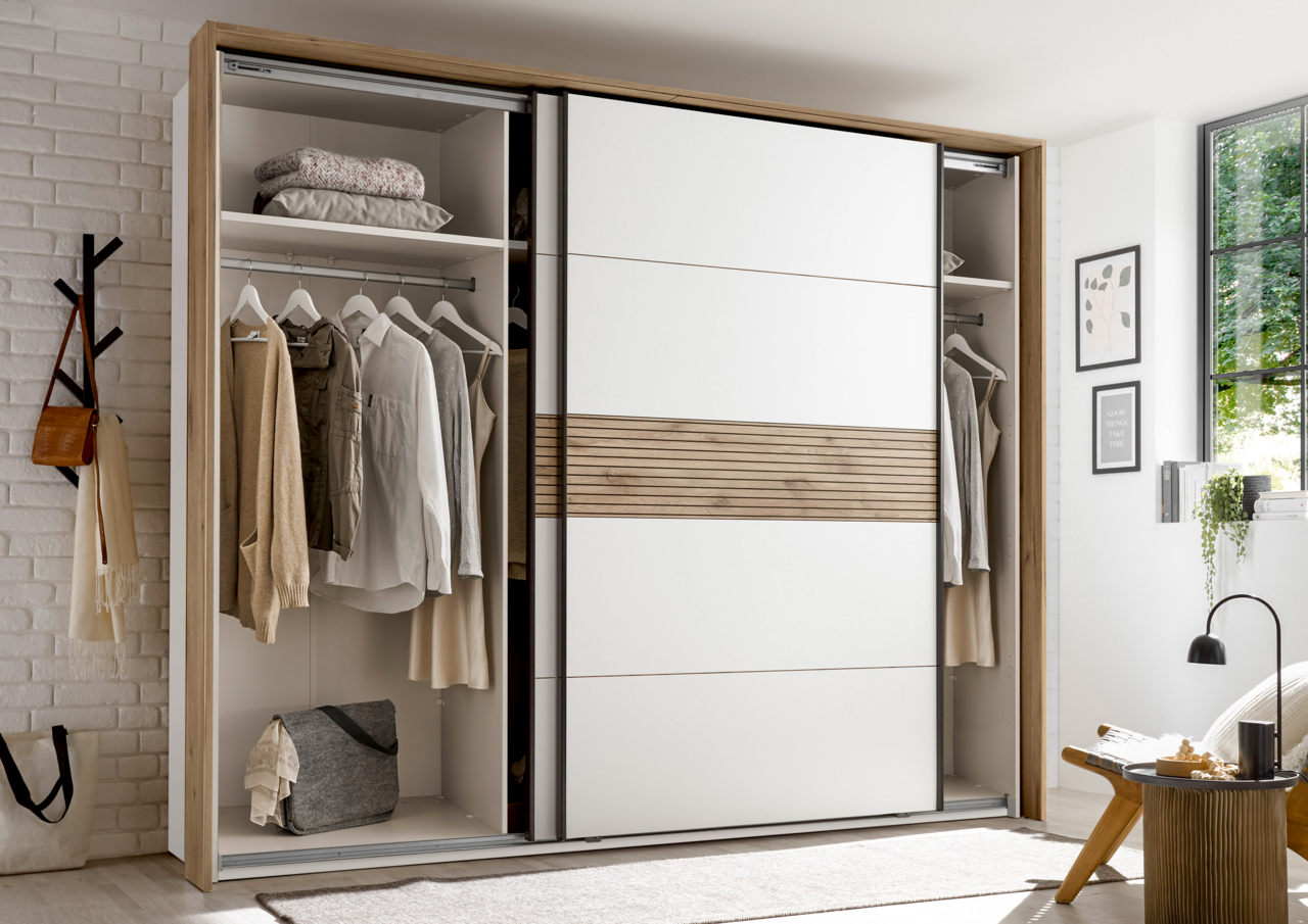 Moderner Schwebetürenschrank mit weißem und holzfarbenem Design, teilweise geöffnet, zeigt Kleidung und Accessoires im Inneren. Perspektive: Frontalansicht.