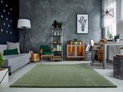 Grüner Teppich Soft Dream ca. 240x290cm in modernem Wohnzimmer mit grauer Couch, grünen Akzenten und Pflanzen, aus der Perspektive des Raumes betrachtet.