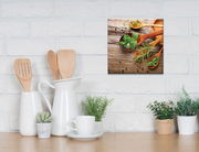 Leinwandbild mit Holzlöffeln und frischen Kräutern auf rustikalem Holztisch, aufgehängt an einer weißen Ziegelwand in einer Küche.