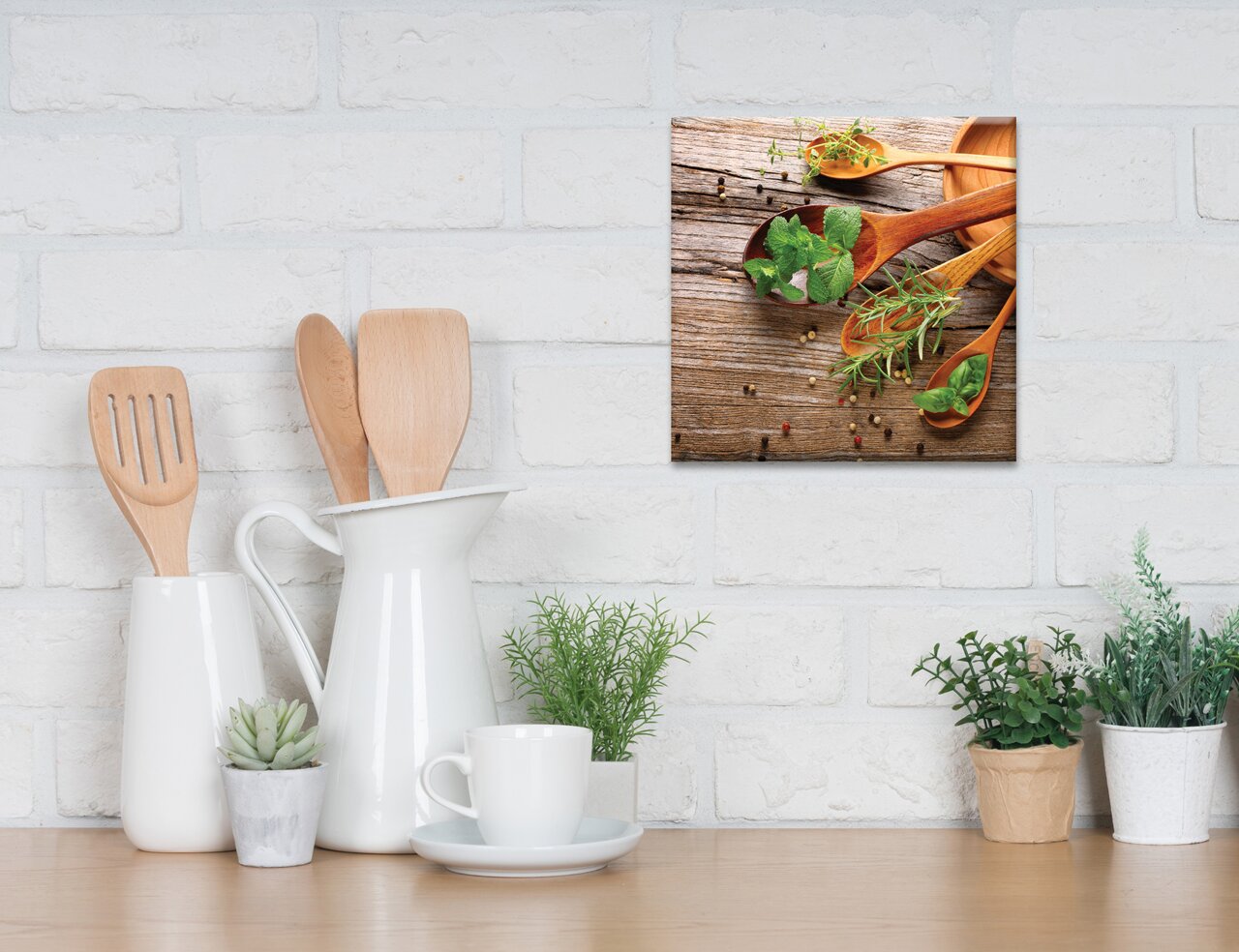 Leinwandbild mit Holzlöffeln und frischen Kräutern auf rustikalem Holztisch, aufgehängt an einer weißen Ziegelwand in einer Küche.