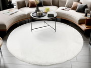 Runder weißer Fellteppich in einem modernen Wohnzimmer, umgeben von einem geschwungenen Sofa und einem runden Couchtisch. Perspektive von oben.