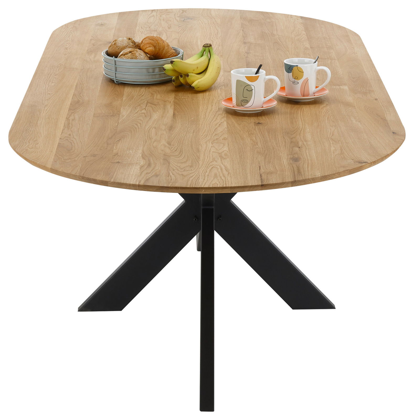 Esstisch mit ovaler Holzplatte und schwarzem Metallgestell, von oben betrachtet, dekoriert mit einem Obstkorb und zwei Tassen.