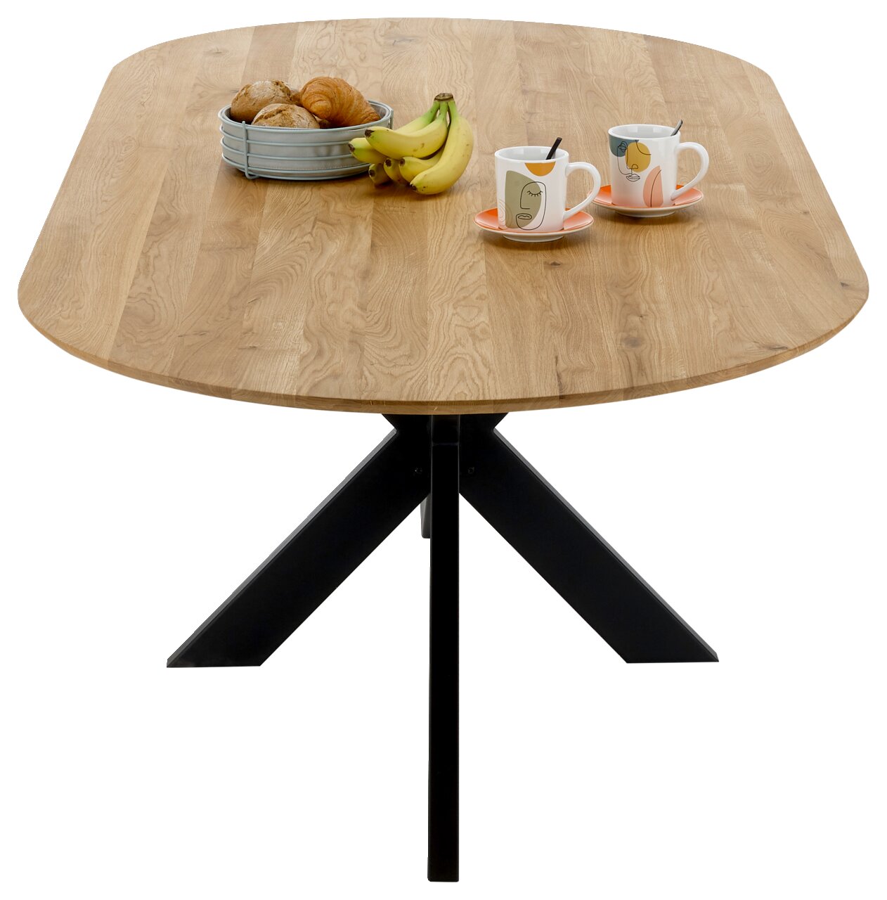 Esstisch mit ovaler Holzplatte und schwarzem Metallgestell, von oben betrachtet, dekoriert mit einem Obstkorb und zwei Tassen.