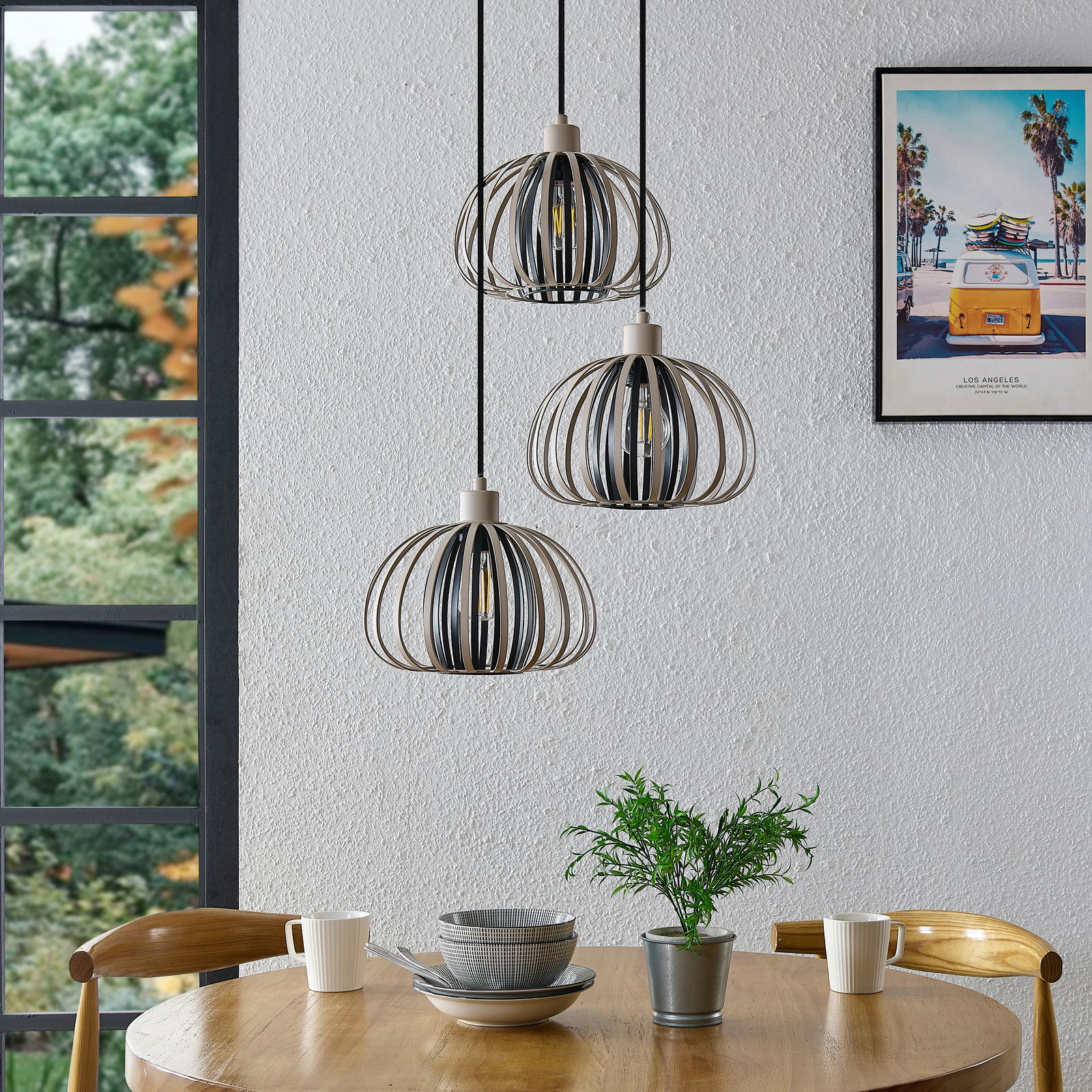 Drei moderne Hängeleuchten in einem Esszimmer, aus der Perspektive von schräg unten fotografiert, mit einem runden Holztisch und Geschirr darunter.