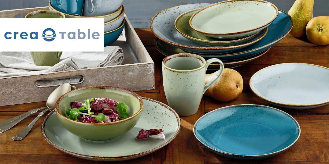 Ein stilvoll gedeckter Tisch mit rustikalem Geschirr in Blau- und Grüntönen der Marke Creatable.
