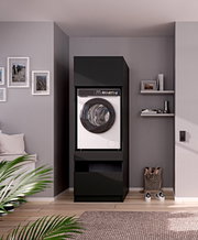 Vooraanzicht: moderne witte voorladerwasmachine met groot rond raam in een zwarte inbouwkast in een stijlvolle woonkamer met planken en schilderijen aan de muur.