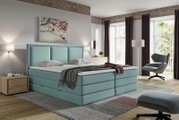Lichtblauw gestoffeerd tweepersoons boxspringbed met hoog, verticaal gecapitonneerd hoofdbord, schuin van voren gezien in een moderne slaapkamer.