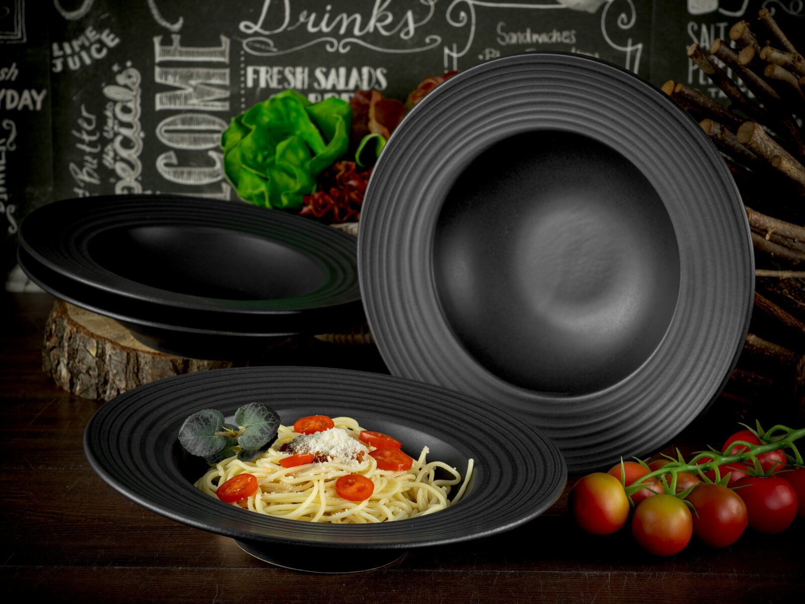 Creatable Pastateller 4-tlg LAVA STONE Schwarzer, mattierter Pastateller mit geriffeltem Rand, im Vordergrund schräg von vorn fotografiert; daneben weitere schwarze Teller, ein Teller aufrecht im Hintergrund.