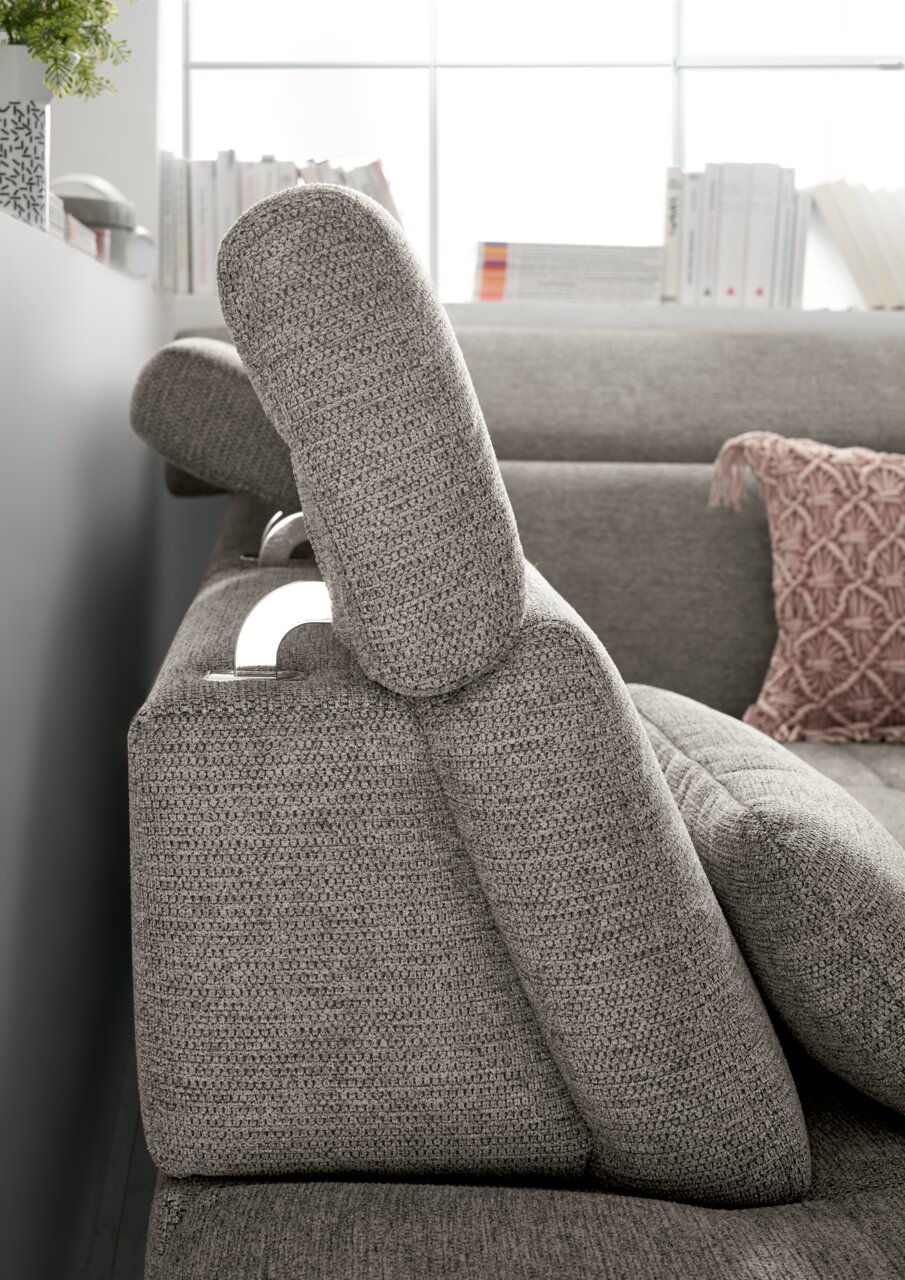 Seitenansicht einer grauen Rundecke mit verstellbarer Kopfstütze und dekorativem Kissen im Hintergrund.