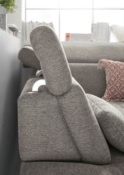 Seitenansicht einer grauen Rundecke mit verstellbarer Kopfstütze und dekorativem Kissen im Hintergrund.