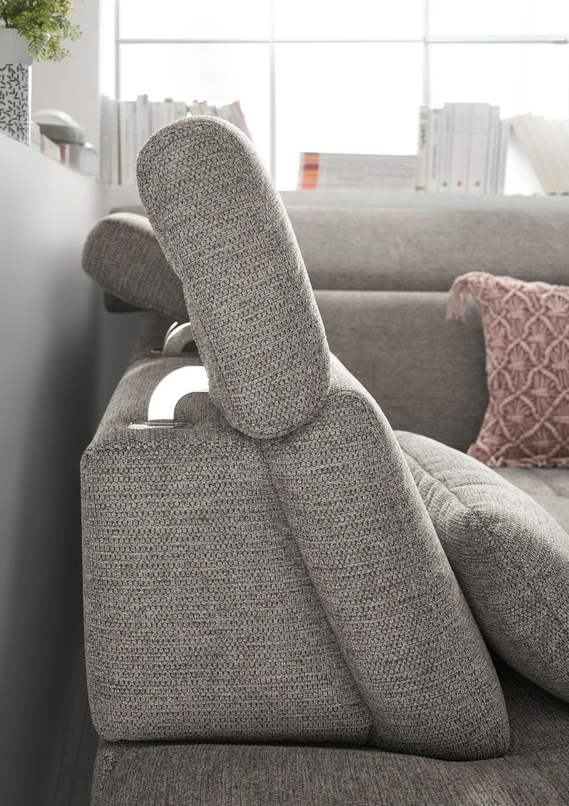 Seitenansicht einer grauen Rundecke mit verstellbarer Kopfstütze und dekorativem Kissen im Hintergrund.