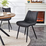 Dunkelgrauer, gepolsterter Esszimmerstuhl mit Stoffbezug und schwarzen Metallbeinen neben rundem Holztisch im Wohnbereich, perspektivisch in schräger Vorderansicht von leicht oben.