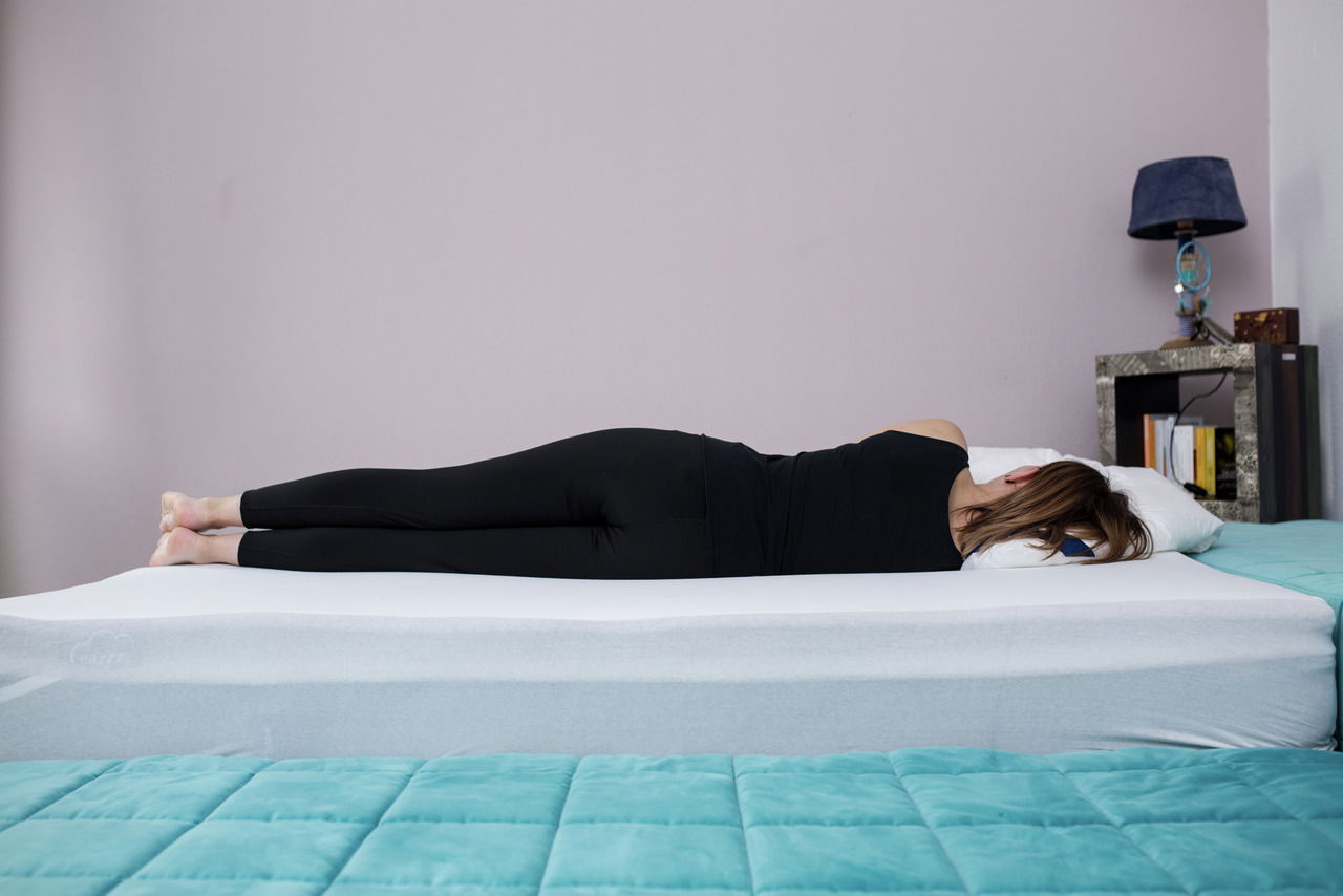 Genius Topper Classic 100*200cm EAZZZY Seitliche Ansicht einer Person, die auf einem EaZzzy Topper Classic 100*200 cm liegt, in einem Schlafzimmer mit Nachttisch und Lampe.