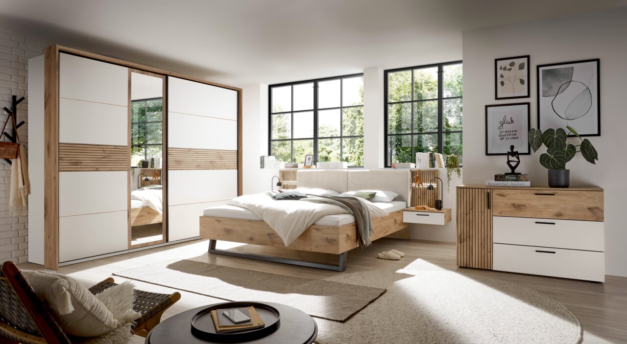 Modernes Schlafzimmer mit Schwebetürenschrank, Bettanlage und Kommode in Holz- und Weißtönen, seitliche Perspektive