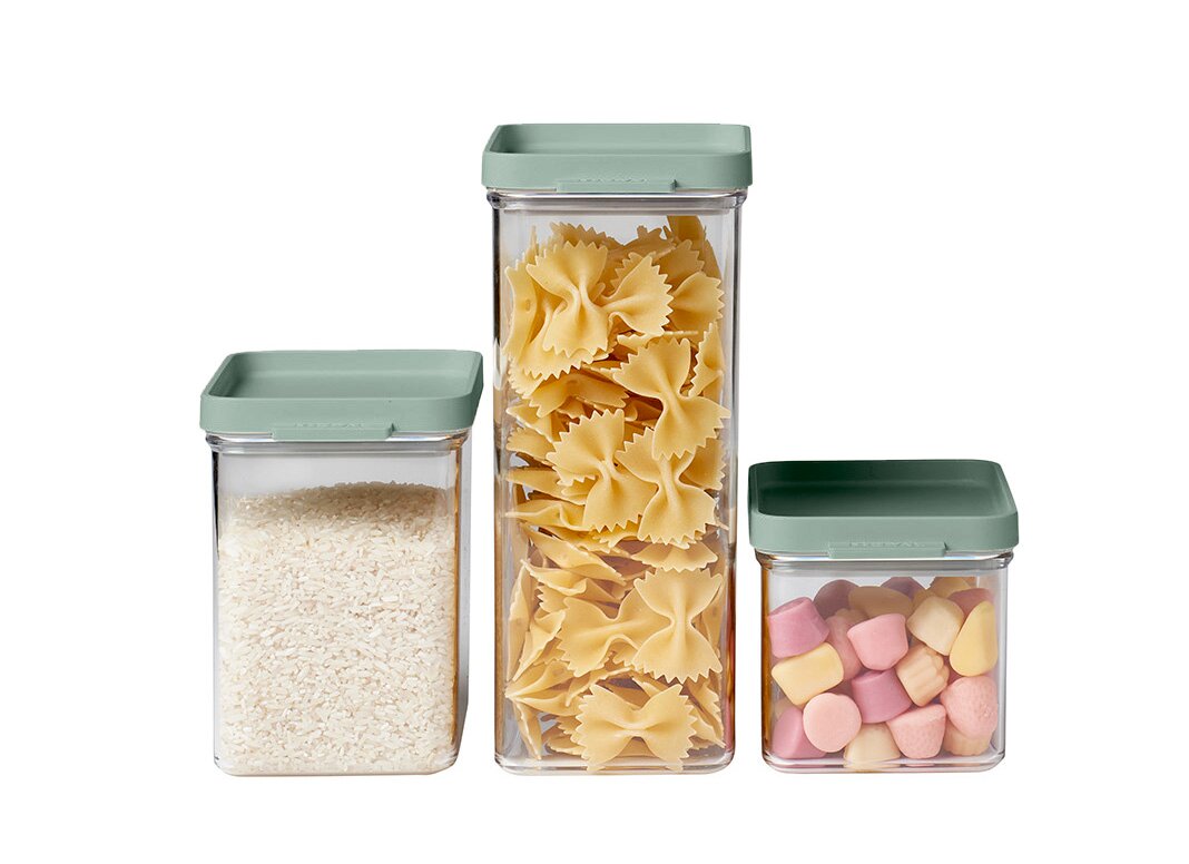 Drei Vorratsdosen in verschiedenen Größen mit grünem Deckel, gefüllt mit Reis, Nudeln und Süßigkeiten, aus frontaler Perspektive.