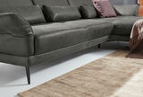 Graues Longchair-Sofa mit schwarzen Beinen, seitliche Perspektive, dekoriert mit Kissen und Decke auf einem hellen Teppich.