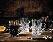 Vier elegante Glühwein-Gläser Noblesse mit Henkel, zwei gefüllt mit Glühwein und Zimtstangen, auf einem rustikalen Holztisch mit Nüssen und Orangenscheiben, seitliche Perspektive.