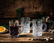 Vier elegante Glühwein-Gläser Noblesse mit Henkel, zwei gefüllt mit Glühwein und Zimtstangen, auf einem rustikalen Holztisch mit Nüssen und Orangenscheiben, seitliche Perspektive.