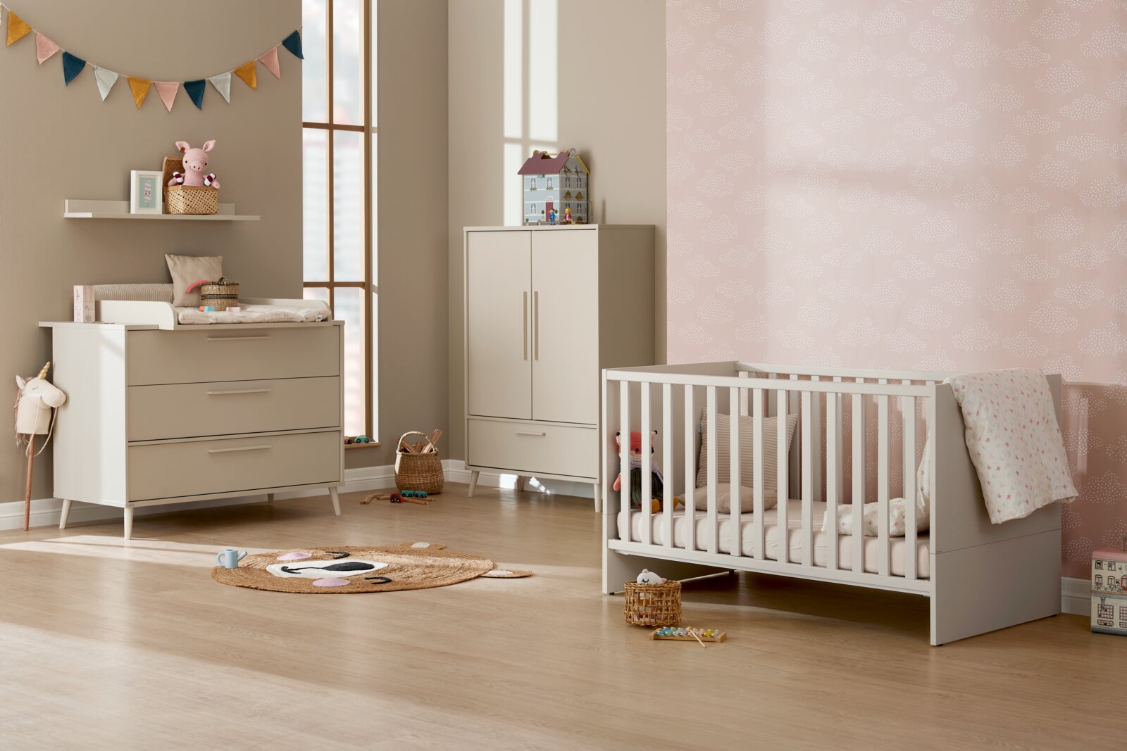 Modernes Babyzimmer mit weiß-grauer Wickelkommode, passendem Kleiderschrank und weißem Gitterbett mit Bettwäsche; Perspektive: Frontalansicht auf die Möbel in einer Raumecke.