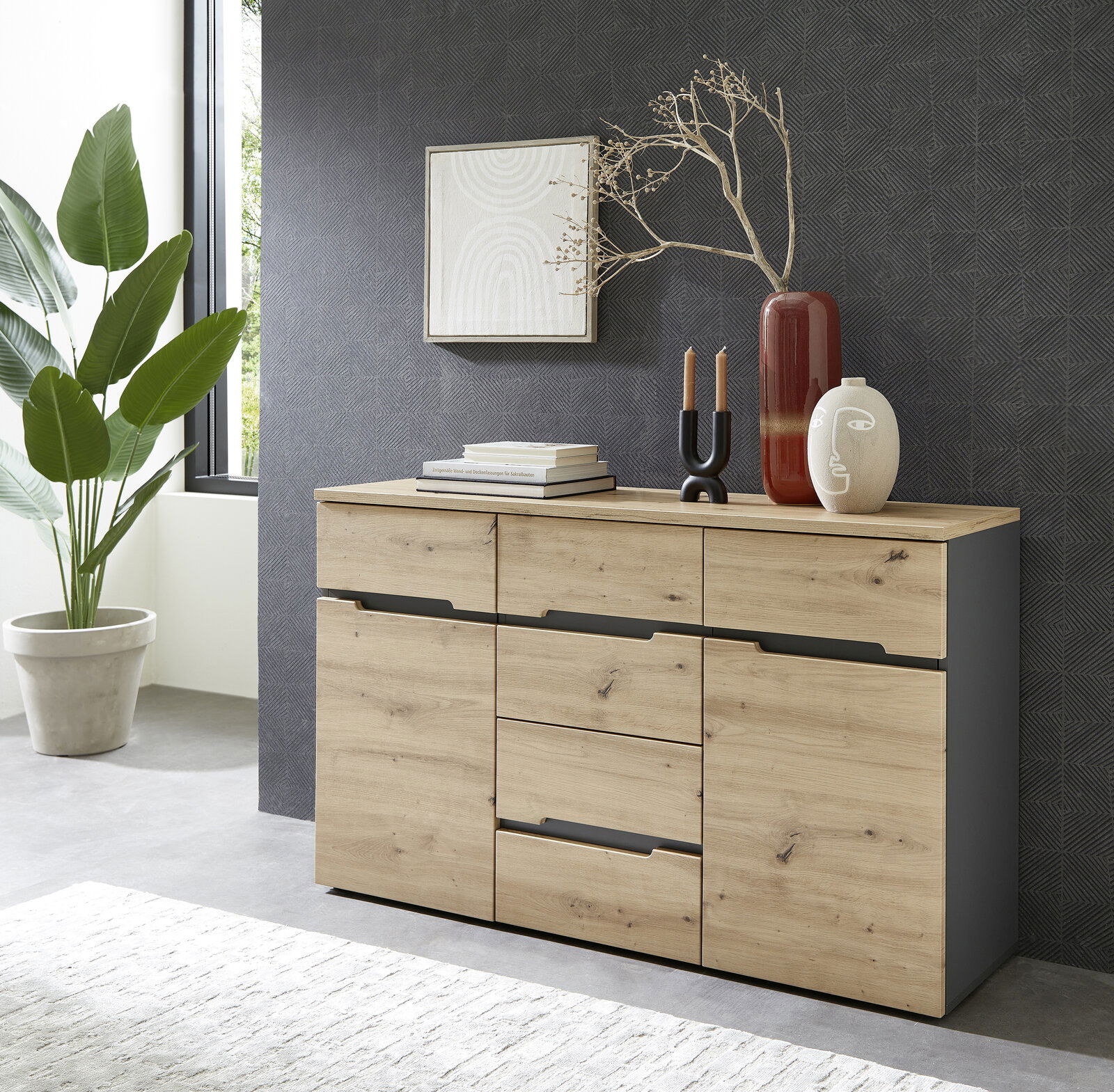 Voleo Dressoir DETROIT Modernes Sideboard aus Holz mit drei Schubladen und zwei Türen, dekoriert mit Vasen und Kerzen, seitliche Perspektive.