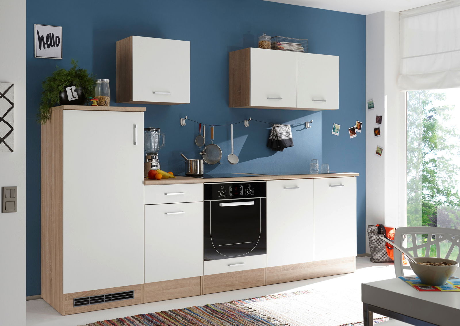 Moderne Küchenzeile mit weißen und holzfarbenen Schränken, blauer Wand im Hintergrund, Perspektive von vorne.