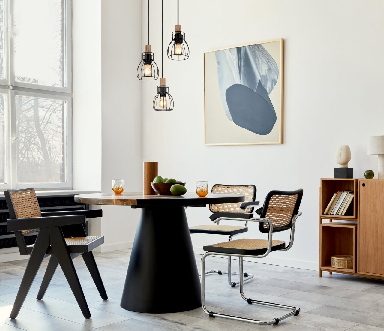 Moderne Hängeleuchte mit drei schwarzen Drahtkäfigen und Holzdetails, von der Decke hängend über einem Esstisch in einem stilvoll eingerichteten Raum, seitliche Perspektive.