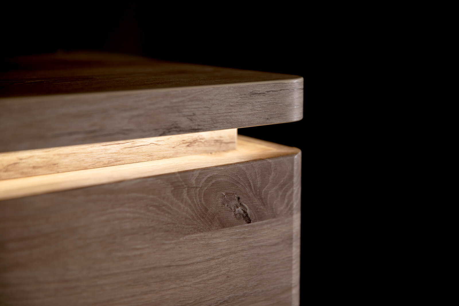 Zurbrüggen TV-Lowboard MODENA Detailaufnahme einer Holzbox mit leicht geöffnetem Deckel, sichtbarer Maserung und abgerundeter Kante vor schwarzem Hintergrund, Perspektive: Nahaufnahme schräg von der Seite