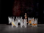 Sechs elegante Whiskybecher aus Kristallglas mit feinem Schliffmuster, frontal auf einem Tisch arrangiert, im Hintergrund ein Cocktailshaker.
