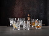 Sechs elegante Whiskybecher aus Kristallglas mit feinem Schliffmuster, frontal auf einem Tisch arrangiert, im Hintergrund ein Cocktailshaker.
