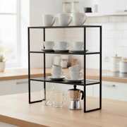 Schwarzes, minimalistisches Küchenregal/Ablagegestell aus Metall mit drei Ebenen auf einer Holzarbeitsplatte, bestückt mit weißen Tassen und Untertassen sowie Gläsern und Espressokanne; Perspektive: frontale leicht schräge Ansicht auf Augenhöhe.