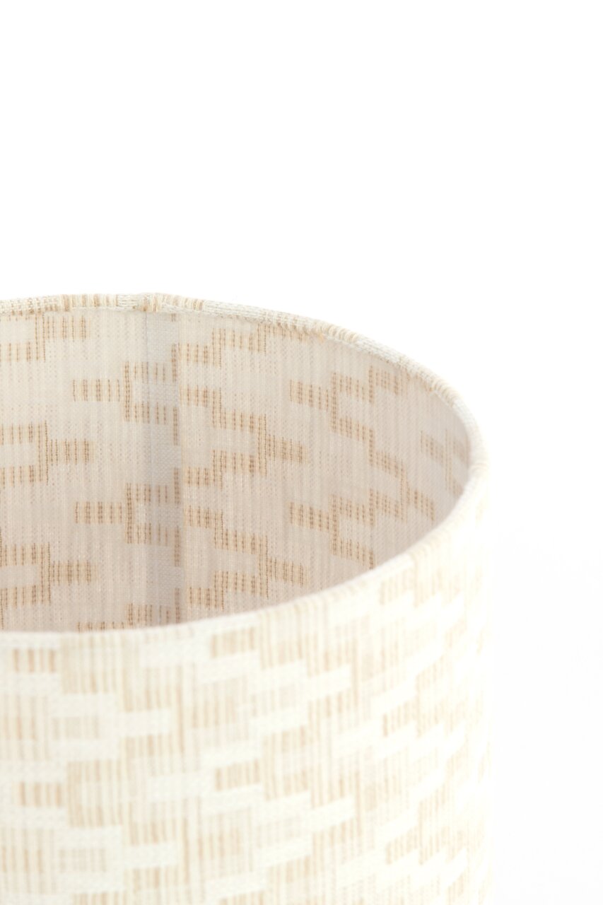 Close-up van een cilindervormige lampenkap met een beige, geweven patroon, gezien van bovenaf.